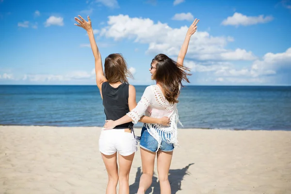 Onnelliset ystävät syleilevät toisiaan nostaen kätensä rannalla — kuvapankkivalokuva