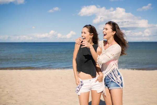 Dos chicas guapas en la playa mirando algo riéndose — Foto de Stock