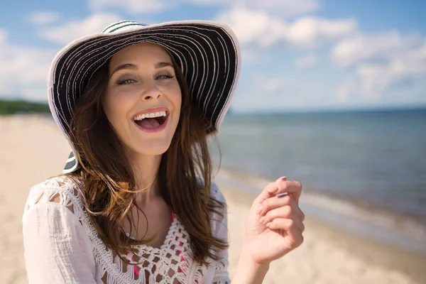 Giovane bella donna in cappello in piedi sulla spiaggia sorridente — Foto Stock