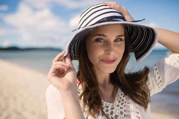 Piękna młoda kobieta trzyma kapelusz na plaży — Zdjęcie stockowe