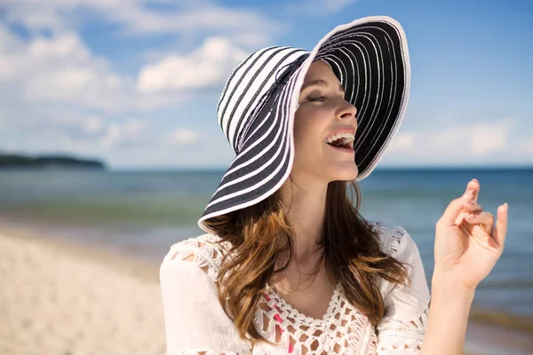Mulher bonita de chapéu em pé na praia rindo — Fotografia de Stock