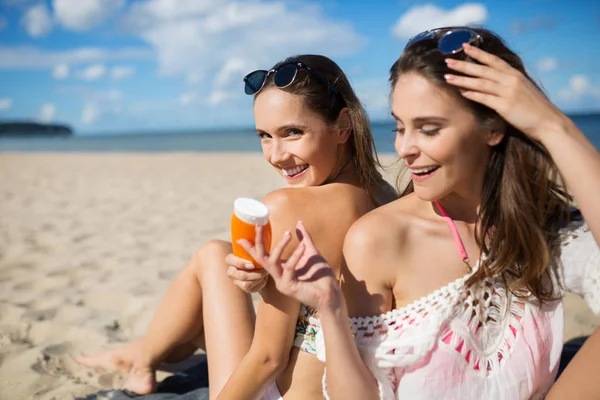 Menina feliz sentado na praia dando óleo bronzeado do sol para seu amigo — Fotografia de Stock