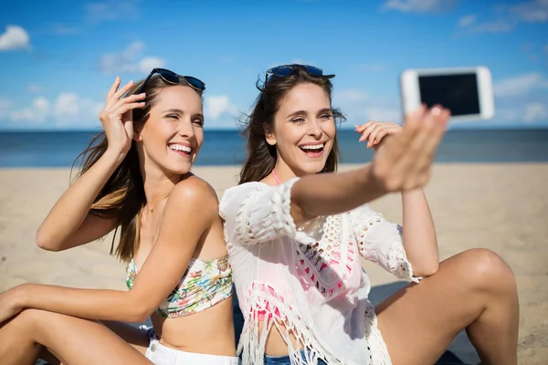 Hübsche Mädchen sitzen am Strand und machen ein Selfie lachend — Stockfoto