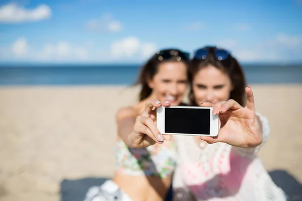 Две девушки на пляже делают селфи на смартфоне — стоковое фото
