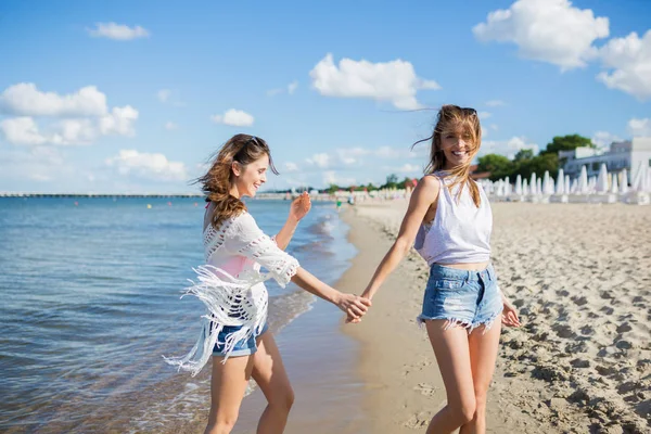 Bella ragazza che cammina sulla spiaggia tenendosi per mano con la sua amica — Foto Stock