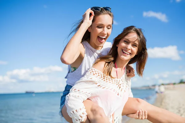 Mulher feliz na praia dando seu amigo piggyback — Fotografia de Stock