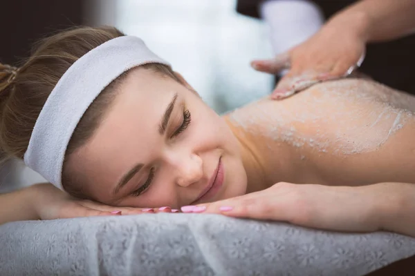 Jonge lachende vrouw krijgen verstevigende suiker scrub therapie op haar b Stockfoto