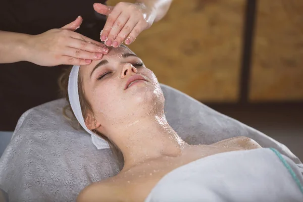 Jonge vrouw tijdens gezicht zout scrub therapie Stockafbeelding