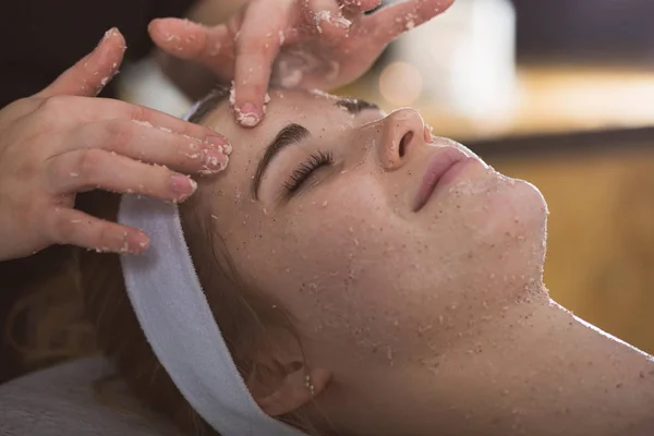 Jonge vrouw tijdens gezicht zout scrub therapie Stockafbeelding