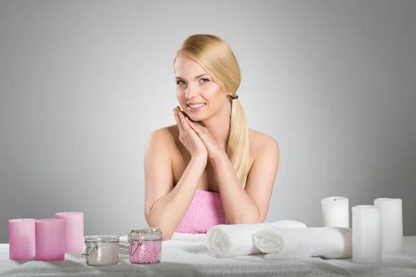 Beautiful woman in towel smiling behind table with spa accessori