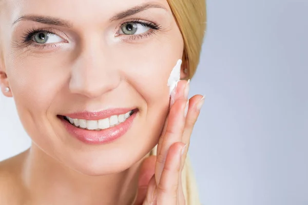 Happy woman applying cream on face looking away — Stock Photo, Image