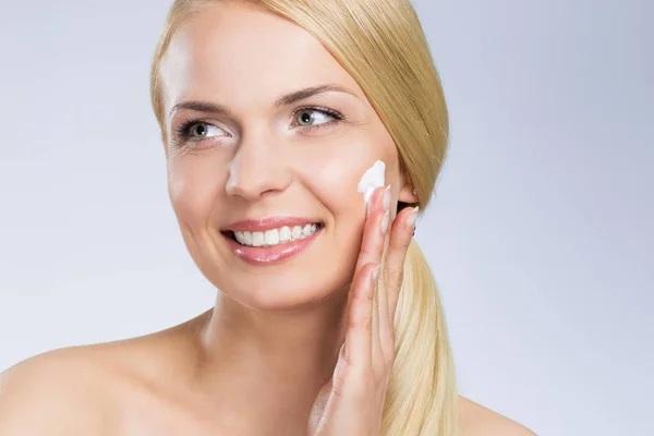Joven mujer feliz aplicando crema en la cara mirando hacia otro lado —  Fotos de Stock
