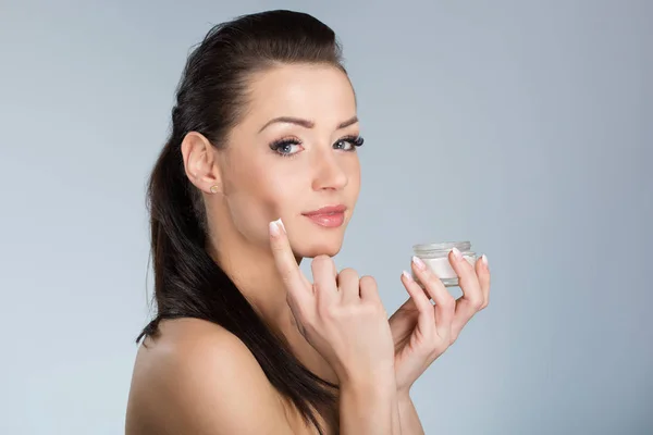 Jovem mulher bonita aplicando creme hidratante no rosto — Fotografia de Stock