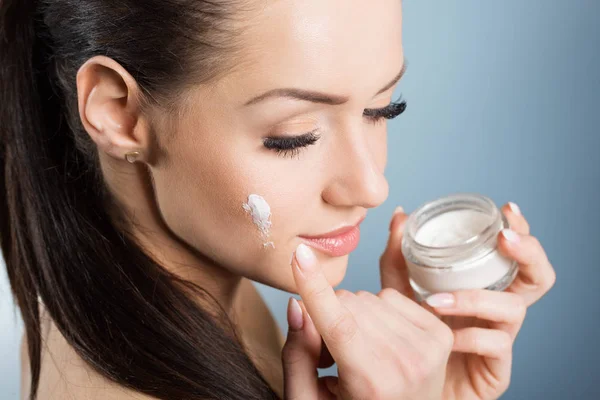 Beautiful woman moistening face with cream — Stock Photo, Image