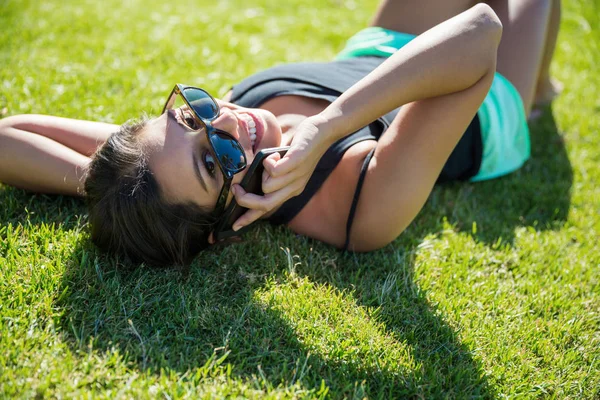 Junge glückliche Frau liegt auf Gras und redet auf Handy — Stockfoto