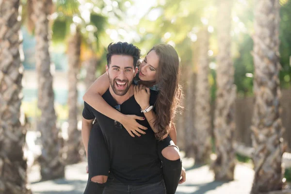 Jovem homem feliz dando a sua namorada um passeio de piggyback — Fotografia de Stock