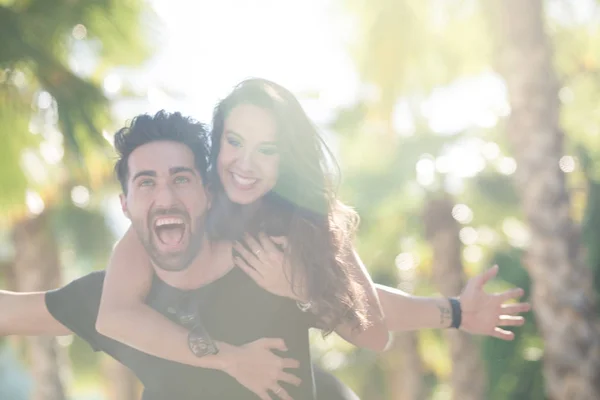 Homem feliz com os braços estendidos dando a sua namorada um porquinho de volta ri — Fotografia de Stock