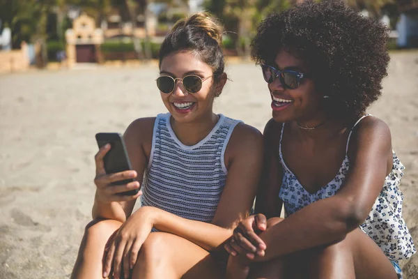Gelukkig meisjes op het strand met behulp van mobiele — Stockfoto