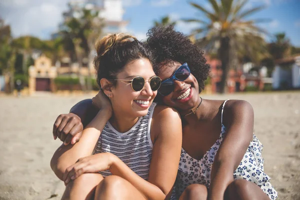 Duas melhores amigas sentadas juntas na praia sorrindo — Fotografia de Stock