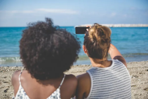 Duas mulheres tirando selfie por celular na praia — Fotografia de Stock