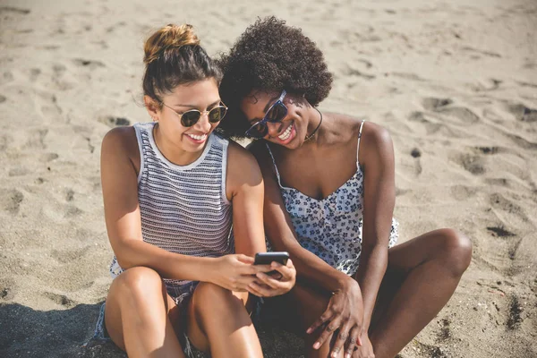 Zwei Freundinnen am Strand mit Handy lächelnd — Stockfoto