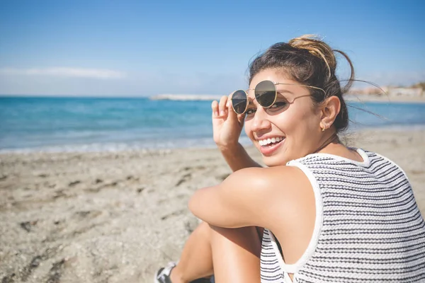 Jolie jeune femme assise sur la plage riant — Photo