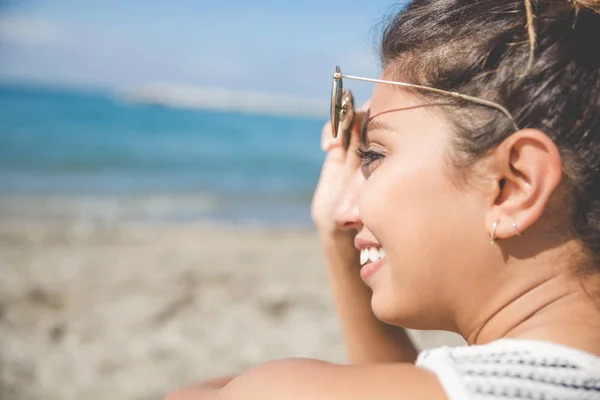 Fiatal csinos nő a gazdaság napszemüveg mosolyogva beach — Stock Fotó