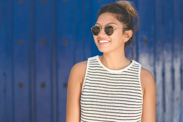 Jeune femme en lunettes de soleil sur fond bleu souriant — Photo