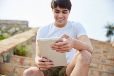 Tablet kullanma dışında merdivenlerde oturan genç mutlu adam