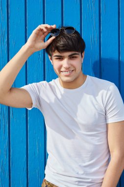 Mutlu adam güneş gözlüğü mavi ahşap duvara tutan genç adam