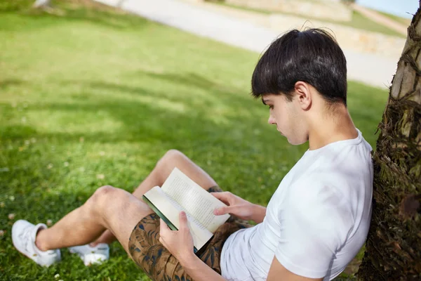 Jovem sentado no livro de leitura de grama — Fotografia de Stock