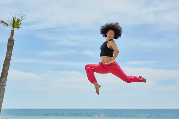 Joven deportista saltando en la playa con las manos en la cintura — Foto de Stock