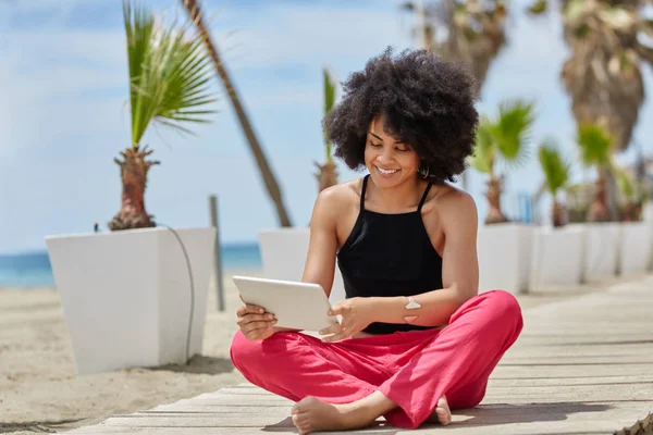 Feliz mujer afroamericana sentada piernas cruzadas usando tableta — Foto de Stock