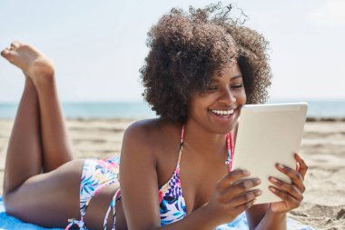 Mutlu afro Amerikalı kadın tablet kumsalda kullanma