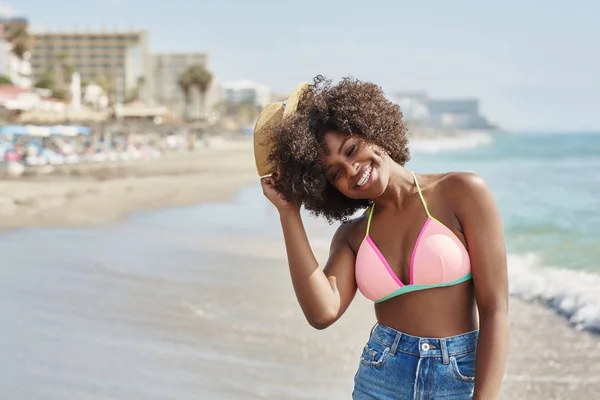 海辺で笑いの頭の上の帽子を保持しているアフロ ・ アメリカ人女性 — ストック写真