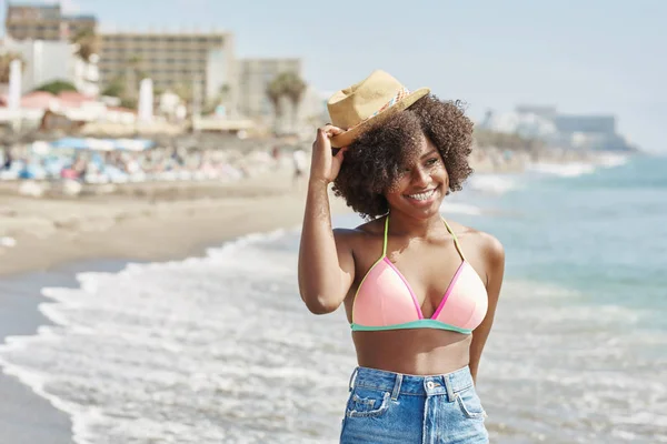 Heureuse femme afro-américaine en bikini tenant un chapeau sur la tête — Photo