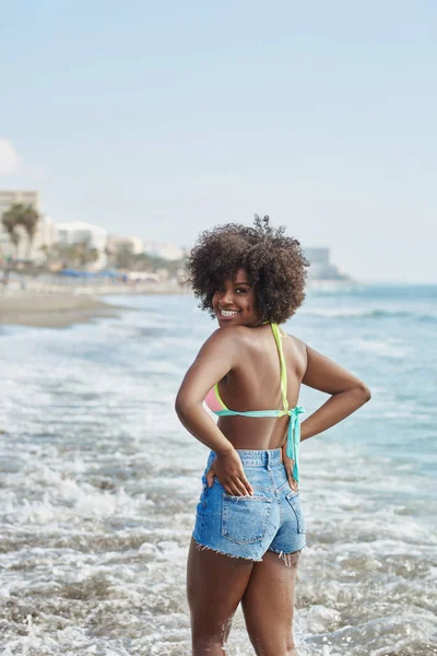 Heureuse femme afro-américaine debout dans l'eau tenant la main dans la poche — Photo