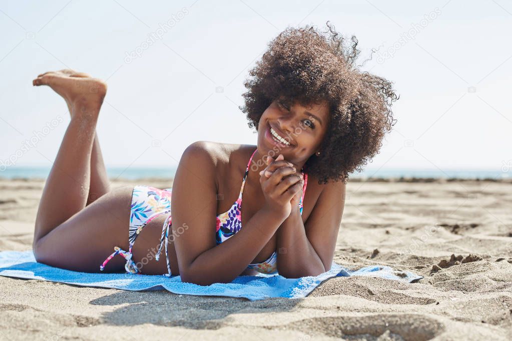 Pretty afro american woman lying on beach smiling