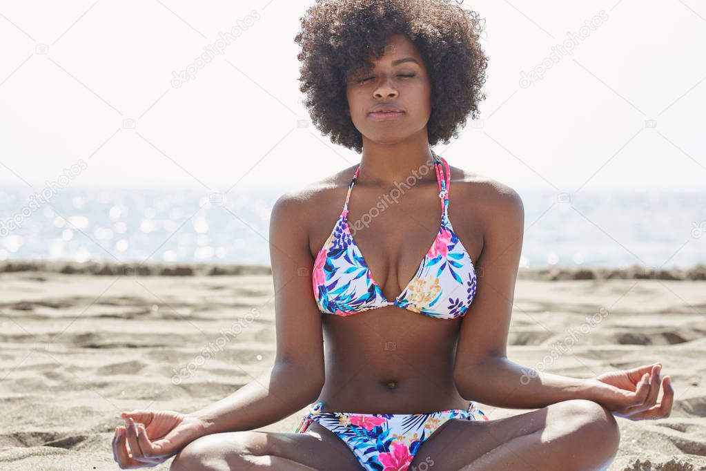 Young afro american woman meditating on beach