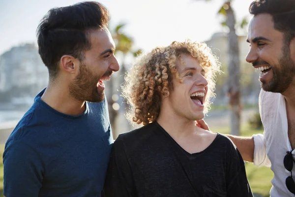 Üç genç adam birlikte gülerek dışarı konuşuyor