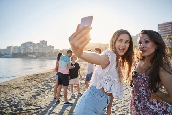 Two male friends taking selfie on beach by smartphone