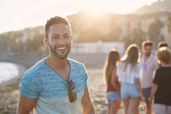 Bello uomo in piedi sulla spiaggia con i suoi amici ridendo — Foto Stock