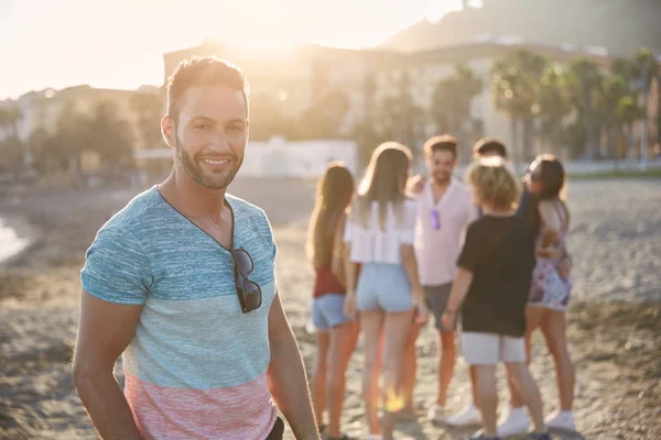 Bonito homem de pé na praia com seus amigos sorrindo — Fotografia de Stock