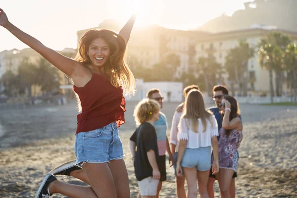Счастливая прыгучая девушка на пляже с группой друзей сзади — стоковое фото
