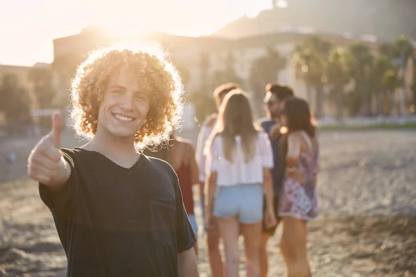Hombre feliz de pie en la playa con amigos mostrando el pulgar hacia arriba — Foto de Stock
