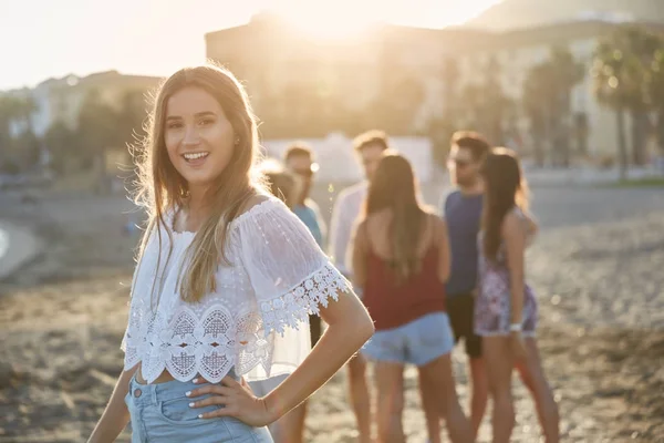Schöne Mädchen mit der Hand auf der Hüfte am Strand stehend mit Freunden b — Stockfoto