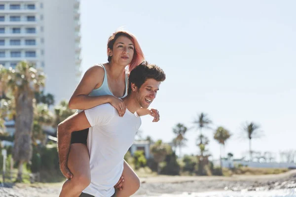 해변에 그의 여자 친구 피기백을 주는 행복 한 사람 — 스톡 사진