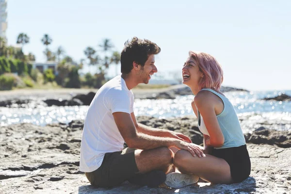 Pareja feliz sentados juntos en la playa riendo —  Fotos de Stock