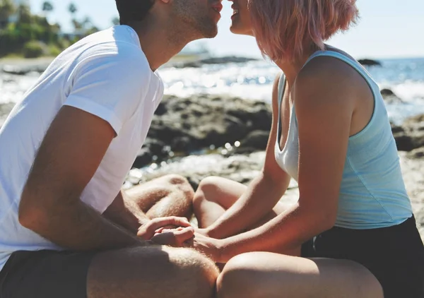 Pareja sentada junta en la playa rocosa besándose — Foto de Stock