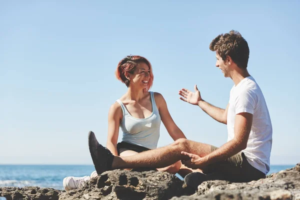 Joyeux couple assis sur une plage rocheuse parlant — Photo